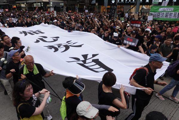 Protesters hold a large white banner with a Chinese idiom expressing how much it hurts, referring to the proposed extradition bill, in Wan Chai, Hong Kong, on June 16, 2019. (Yu Gang/The Epoch Times)