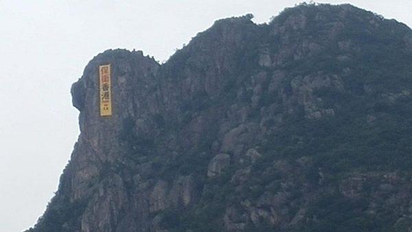 Yellow banner with the Chinese characters "Defend Hong Kong” seen hanging from Lion Rock above Kowloon, Hong Kong, on June 16, 2019. (Zhang Xiaohong/The Epoch Times)