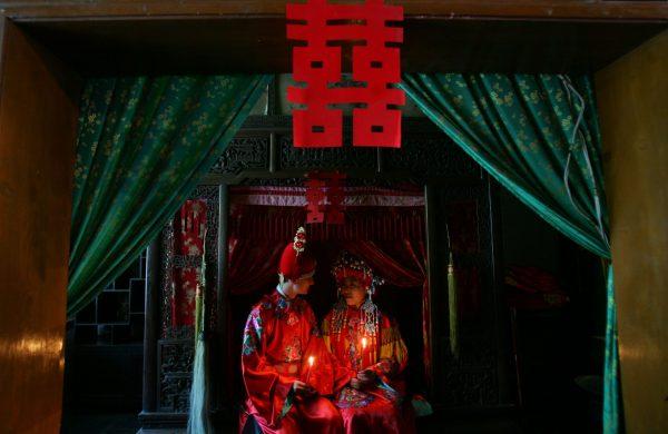 A newlywed couple, the groom from France and bride from China, sit on a bed in the bridal chamber. The character above means "Double Happiness." (China Photos/Getty Images)