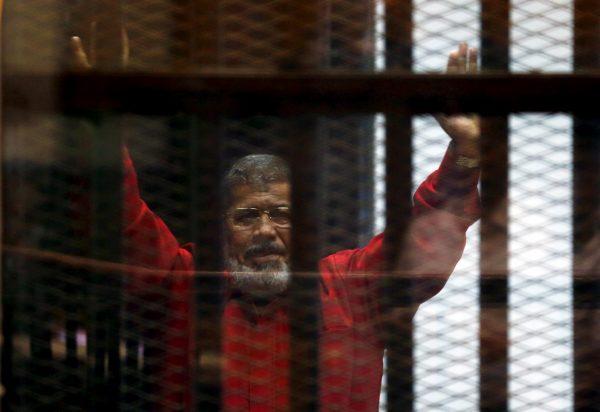 Egypt's deposed President Mohamed Morsi greets his lawyers and people from behind bars at a court wearing the red garb of a prisoner sentenced to death, during his court appearance in Cairo on June 21, 2015. (Amr Abdallah Dalsh/File Photo via Reuters)