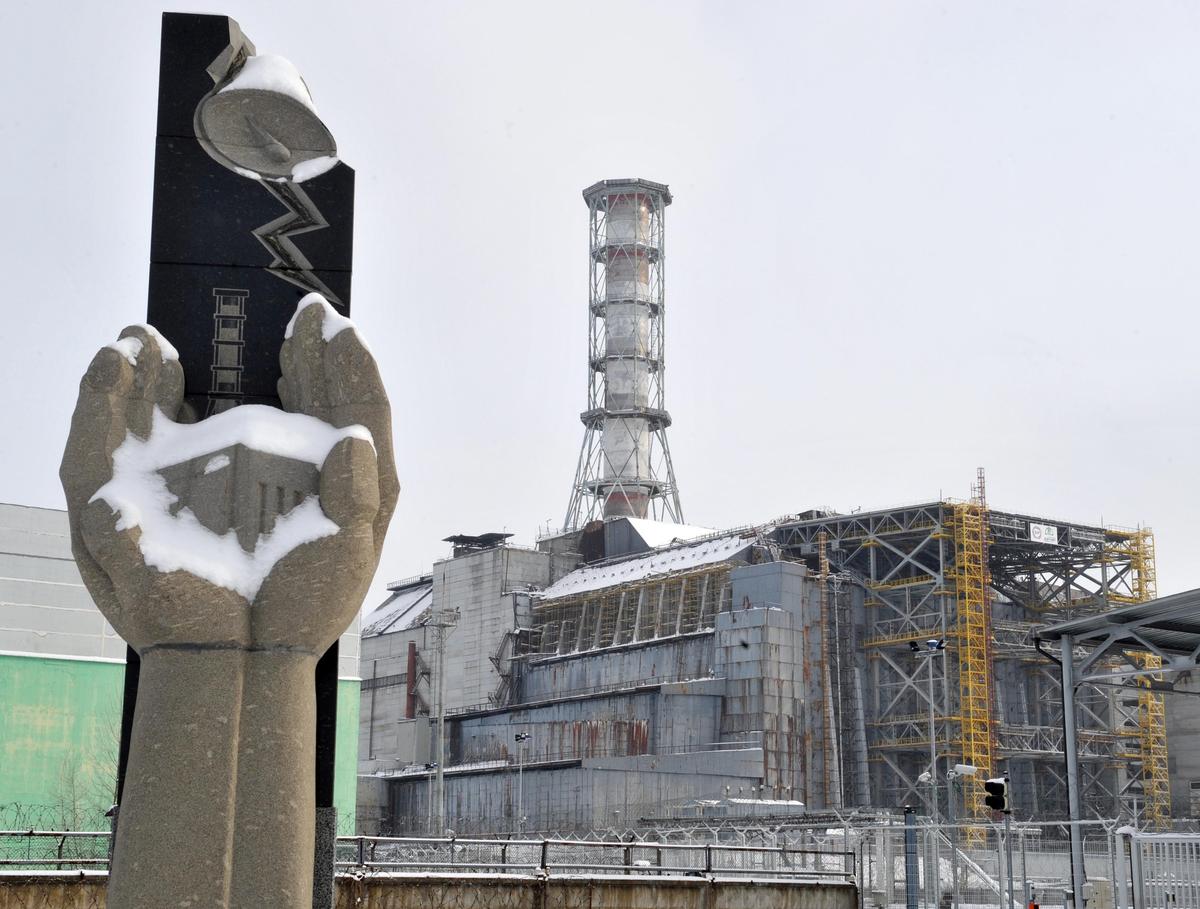 A memorial for the Chernobyl Nuclear Disaster victims is pictured in front of the sarcophagus covering the destroyed 4th power block of Chernobyl's nuclear power plant. (©Getty Images | <a href="https://www.gettyimages.com/detail/news-photo/memorial-for-the-chernobyl-nuclear-disaster-victims-is-news-photo/110964286?adppopup=true">SERGEI SUPINSKY</a>)