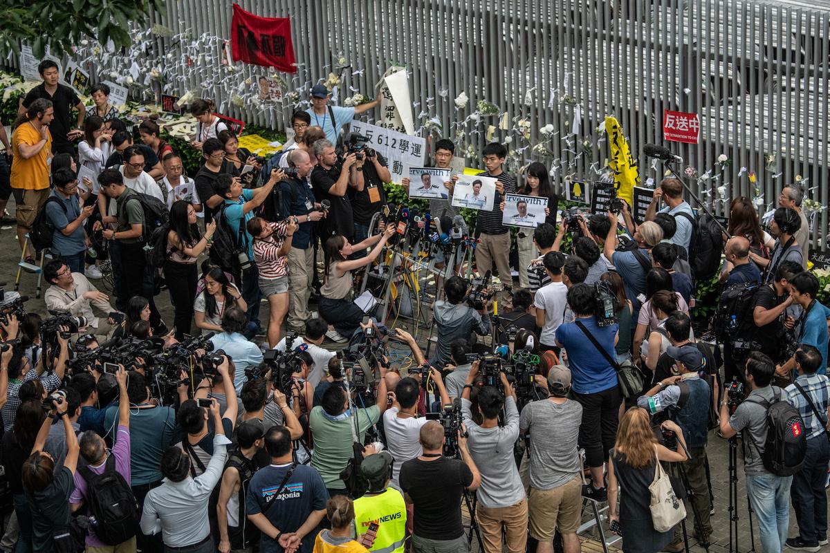 Pro-democracy activist Joshua Wong (C-R) holds a protest poster as he speaks to members of the media outside the Legislative Council building following a press conference by Hong Kong Chief Executive Carrie Lam in Hong Kong on June 18, 2019. (Carl Court/Getty Images)