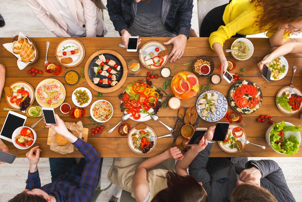 A table full of food and friends and everyone's on their phone (Illustration - Shutterstock | <a href="https://www.shutterstock.com/image-photo/online-dinner-gadget-device-addiction-friends-676437394?studio=1">Prostock-studio</a>)