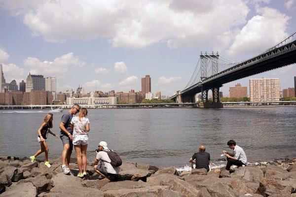 People relax near the Manhattan Bridge, with the bridge in the background on Aug. 19, 2014. (Spencer Platt/Getty Images)