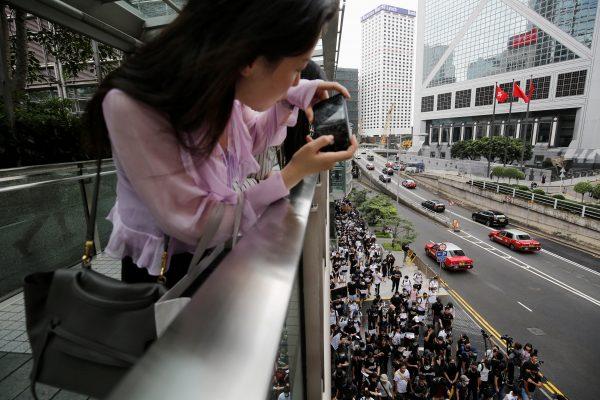 A office worker takes photos of the activists' march to major international consulates in an attempt to rally foreign governments' support for their fight against a controversial extradition bill in Hong Kong, China on June 26, 2019. (Ann Wang/Reuters)