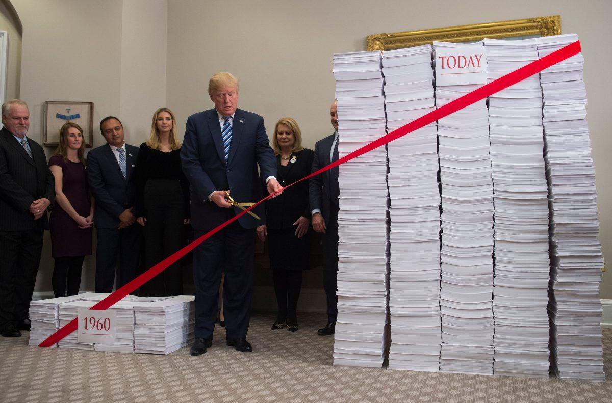 President Donald Trump uses gold scissors to cut a red tape tied between two stacks of papers representing the government regulations of the 1960s (L) and the regulations of today (R) after he spoke about his administration's efforts in deregulation in the Roosevelt Room of the White House on Dec. 14, 2017. (Saul Loeb/AFP/Getty Images)