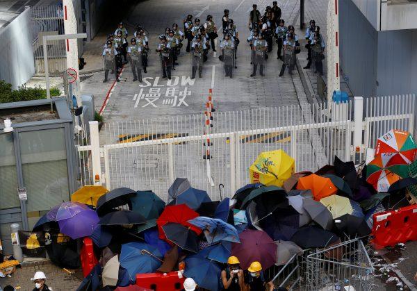Anti-extradition bill protesters use umbrellas to build a barricade while riot police stand guard on the Legislative Council compound during the anniversary of Hong Kong's handover to China in Hong Kong, July 1, 2019. (Thomas Peter/Reuters)
