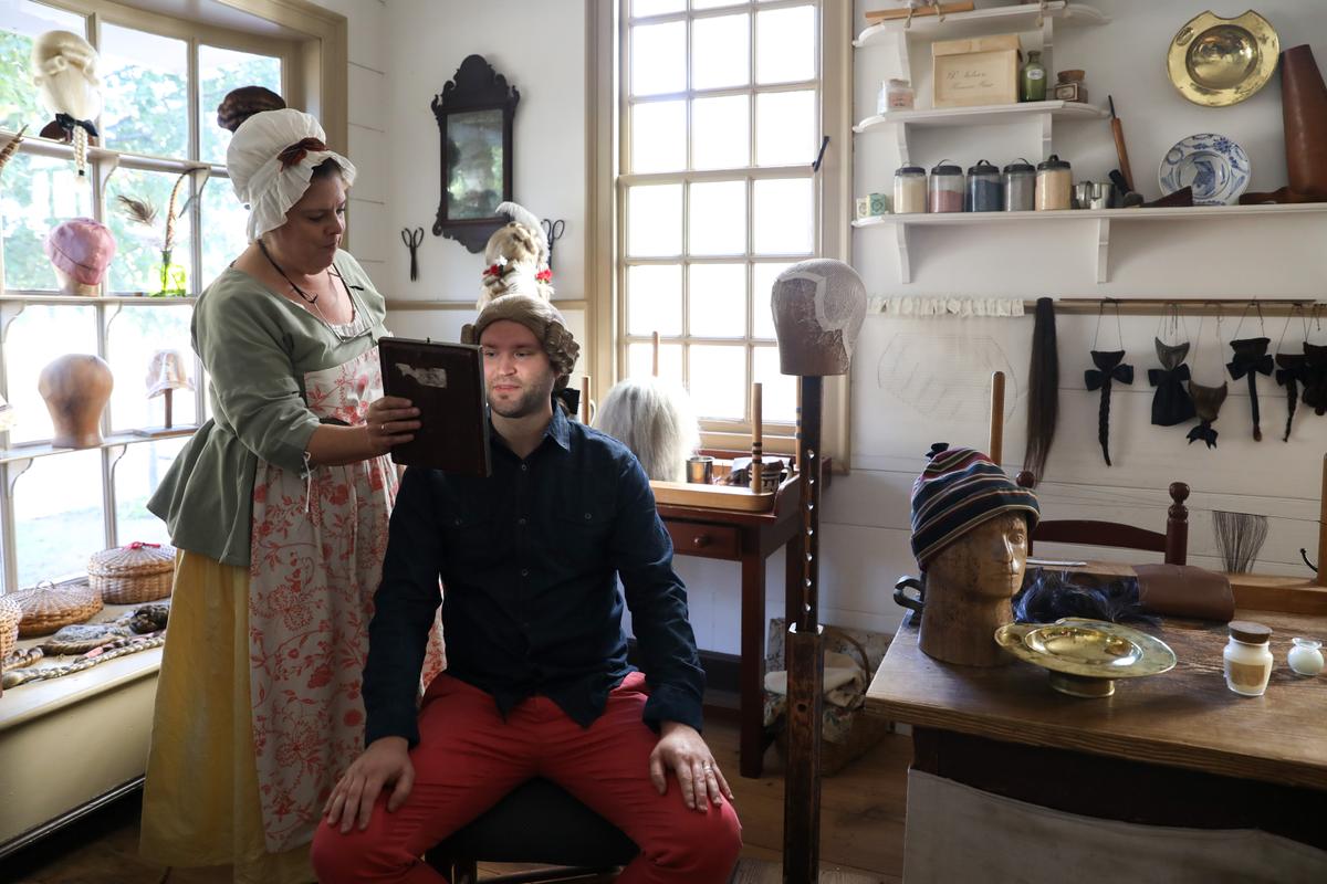 A 21st century visitor dons a wig at Mary's wigmaker shop. The character of Mary is interpreted by Betty Myers. (Samira Bouaou/The Epoch Times)
