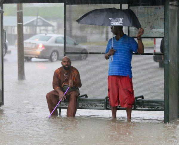 Residents sit under a bus shelter along a flooded Broad Street as heavy rain falls in New Orleans, on July 10, 2019. (David Grunfeld/The Advocate via AP)