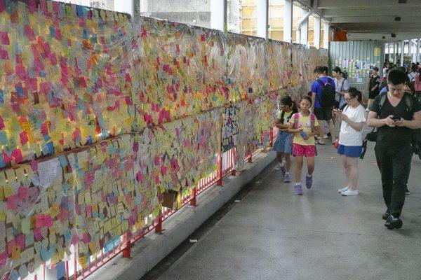Passengers walk by a “Lennon Wall", which contains messages of support for pro-democracy protesters, in the Hong Kong suburb of Tsuen Wan on July 12, 2019. (Yu Kong/The Epoch Times)