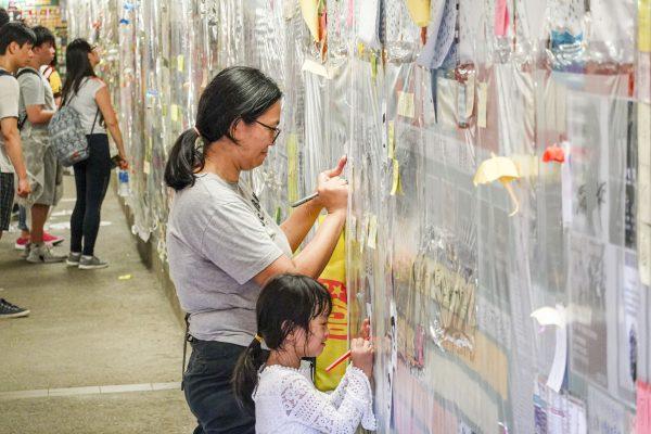 People write notes against the proposed extradition bill before sticking them onto a sign board, reminiscent of the Lennon Wall seen during the 2014 pro-democracy protests, in the Tai Po district of Hong Kong on July 12, 2019. (Yu Kong/The Epoch Times)