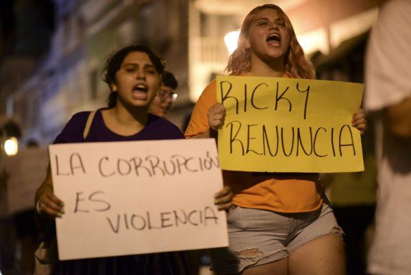 Demonstrators holding signs that read in Spanish "Corruption is violence" and "Ricky renounce", protest near the executive mansion denouncing a wave of arrests for corruption that has shaken the country and demanding the resignation of Gov. Ricardo Rosello, in San Juan, Puerto Rico on July 11, 2019. (Carlos Giusti/AP)