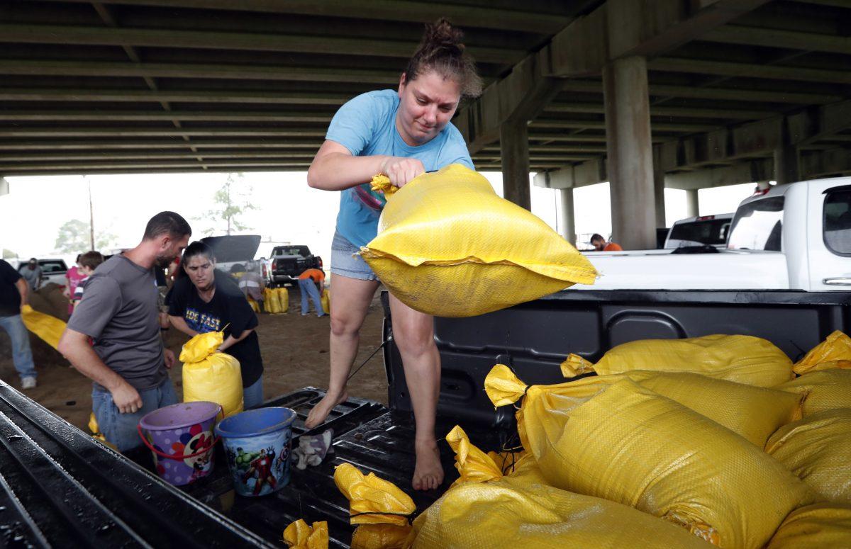 Tiffany Delee tosses a filled sandbag into the back of the family truck, while her husband Mike Delee, left, readies to tie up another bag, in Morgan City, La., July 12, 2019. The Delee's will use the bags to help protect their grandmother's house in the city. (AP Photo/Rogelio V. Solis)