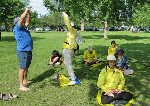 Kathy Gillis shows a passerby the Falun Dafa exercises while others in the group meditate at Mooney’s Bay Park on June 22, 2019. (Courtesy of Kathy Gillis)