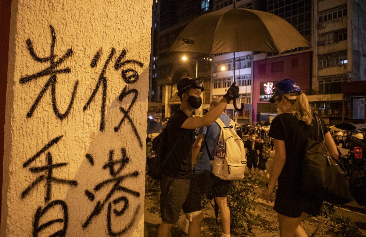 Protesters paint sprayed words "Free Hong Kong" near the Hong Kong Liaison Office on July 28, 2019. (Yu Gang/The Epoch Times)