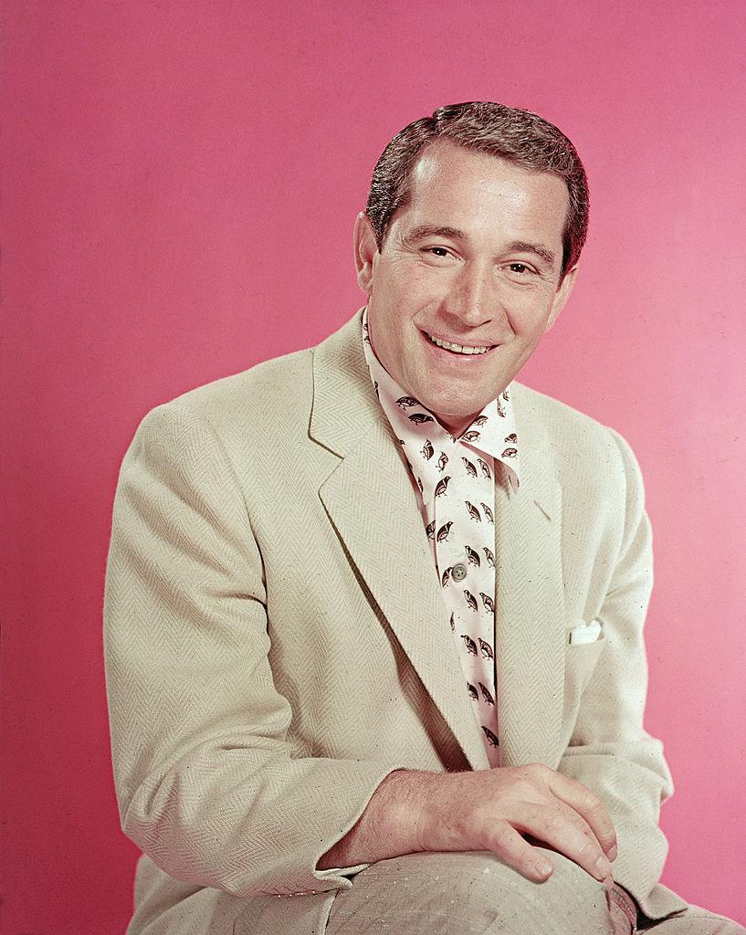 Portrait of a smiling Perry Como, perched in a shirt and tan jacket in the mid-1950s (©Getty Images | <a href="https://www.gettyimages.com.au/detail/news-photo/portrait-of-popular-american-singer-perry-como-as-he-sits-news-photo/53203755">Hulton Archive</a>)