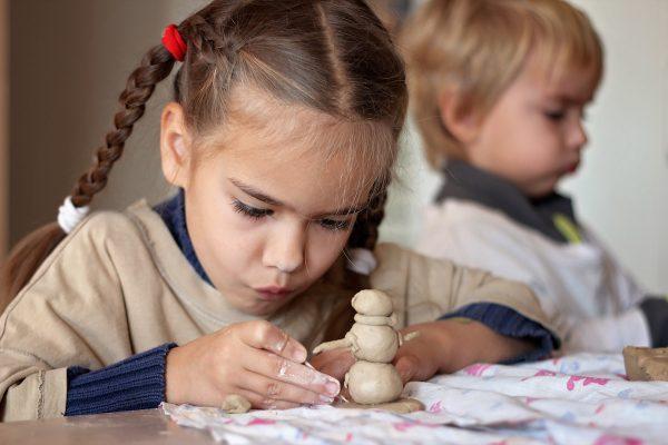 Girl is playing with modeling clay in pottery workshop. (Shutterstock)