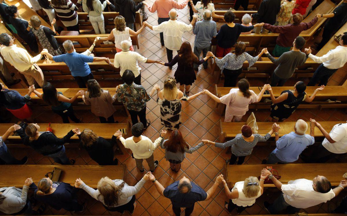 Churchgoers hold hands as they sing during a morning service at St. Pius X Church in El Paso, Texas, on Aug. 4, 2019. (Vernon Bryant/The Dallas Morning News via AP)
