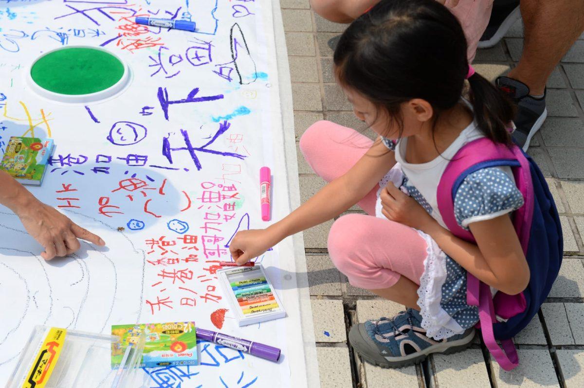 A girl drawing on a large poster in support of Hong Kong protesters at a rally in the city's central business district, on Aug. 10, 2019. (Song Bilong/The Epoch Times)