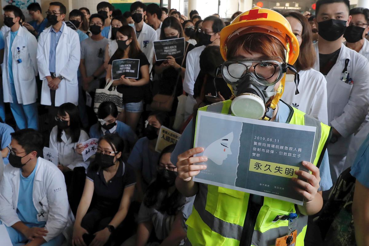 Medical staff take part in a protest against police brutality on the protesters, at a hospital in Hong Kong, China on Aug. 13, 2019. Demonstrators have in recent days focused on their demand for an independent inquiry into what they call the police’s abuse of power and negligence. That followed reports and circulating video footage of violent arrests and injuries sustained by protesters. The sign, front right, reads " Police fired bean bag round to a medical worker and she lost her eye." (Kin Cheung/AP)