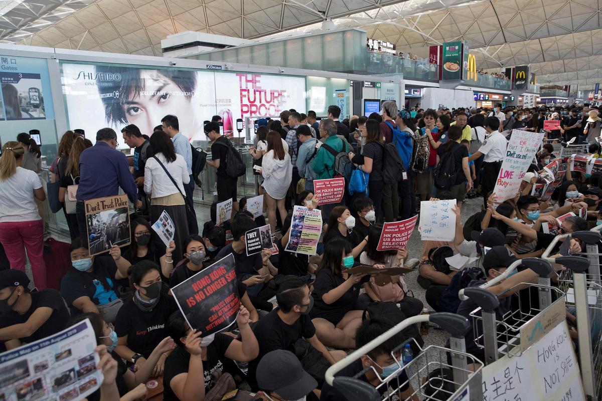 Traveller walk past protesters hold placards and posters take part in a sit-in rally near the departure gate of the Hong Kong International airport in Hong Kong, China on Aug. 13, 2019. (Vincent Thian/AP)