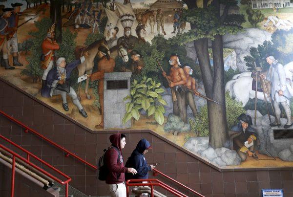 A pair of students walk past a historic mural that includes slaves and a dead Native American at George Washington High School in San Francisco. (Yalonda M. James/San Francisco Chronicle via AP)