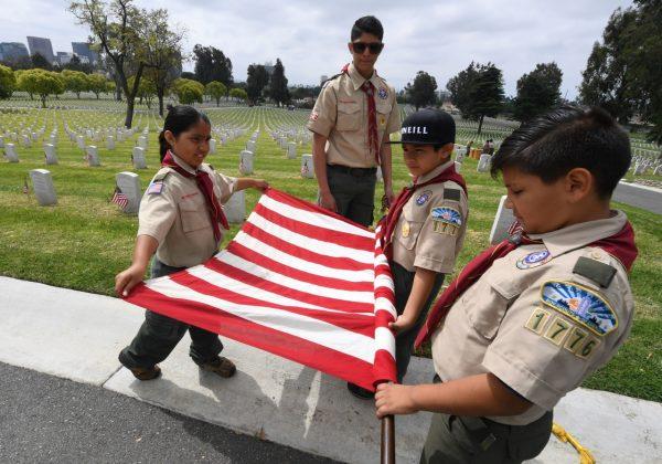 Boy Scouts prepare a US flag besides the graves of war veterans during the annual 'Flag Placement ceremony' to honor the fallen for Memorial Day at the Los Angeles National Cemetery, Calif., on May 25, 2019. (Mark Ralston/AFP/Getty Images)