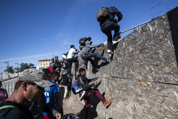 A group of Central American migrants—mostly from Honduras—climb a fence as they try to reach the U.S.–Mexico border near the El Chaparral border crossing in Tijuana, Baja California State, Mexico, on Nov. 25, 2018. (Pedro Pardo/AFP/Getty Images)