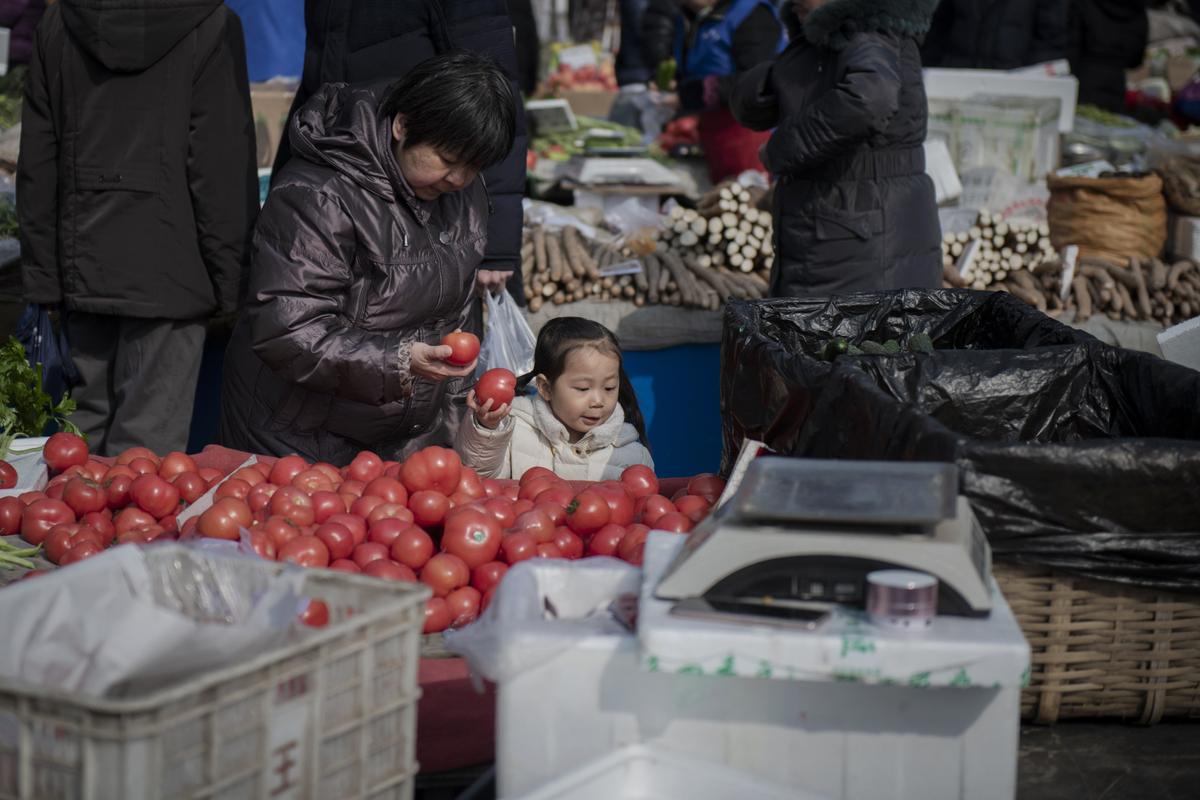 A young girl helps a woman to choose tomatoes at a market in Beijing on Feb. 27, 2019. (Nicolas Asfouri/ AFP/Getty Images)