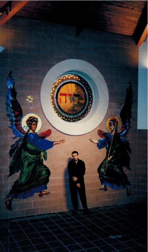 Niko Chocheli stands in front of his icons of two archangels. These larger-than-life angels, painted in acrylic and gold leaf on canvas, were part of a mural project at St. Basil the Great church in Kimberton, Pennsylvania. (Kristen Chocheli)