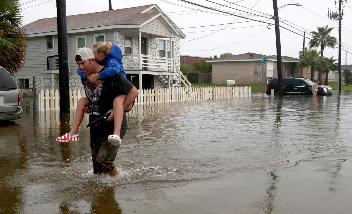 Terry Spencer carries his daughter, Trinity, through high water on 59th Street near Stewart Road in Galveston, Texas Sept. 18, 2019, as heavy rain from Tropical Depression Imelda caused street flooding on the island. (Jennifer Reynolds/The Galveston County Daily News via AP)