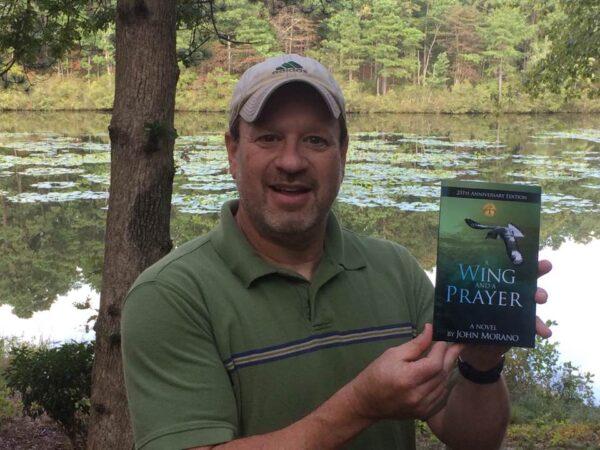 John Morano holding the first novel of the Eco-Adventure series, "A Wing and A Prayer." (Mark Ludak)