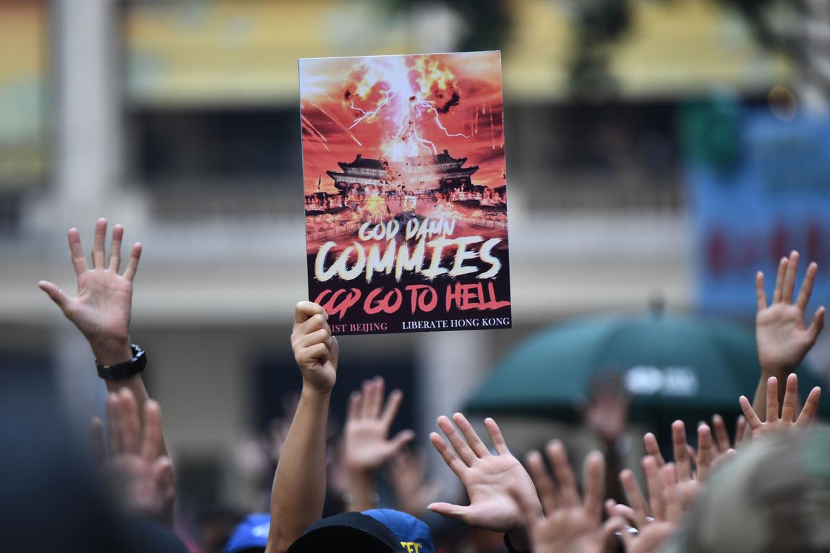 A protester holds up a placard as others hold up their hands to signify their five demands at a rally in the Wanchai district of Hong Kong on Oct. 1, 2019, the 70th anniversary of the Chinese communist regime's founding. (Anthony Wallace/AFP/Getty Images)