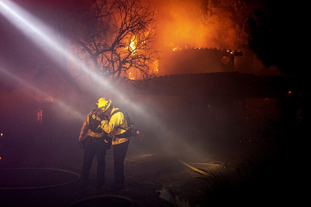 Firefighters recoil from smoke and heat from a fully engulfed house on Jolette Way in Granada Hills North, Calif., early Friday morning, Oct. 11, 2019. (David Crane/The Orange County Register via AP)