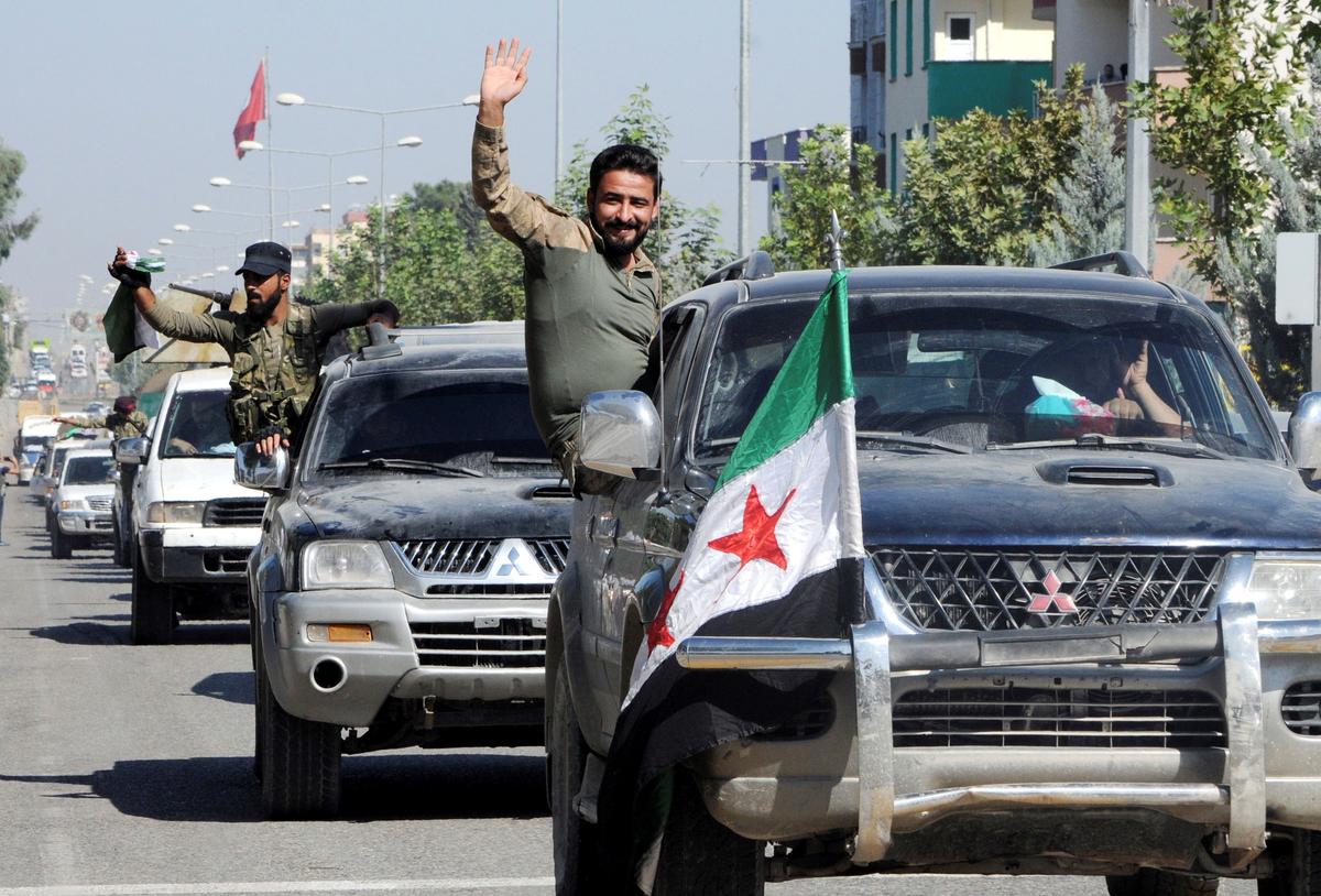Members of Syrian National Army, wave as they drive to cross into Syria in the Turkish border town of Akcakale in Sanliurfa province, Turkey, on Oct. 10, 2019. (Hasan Kirmizitas/Demiroren News Agency/via Reuters)