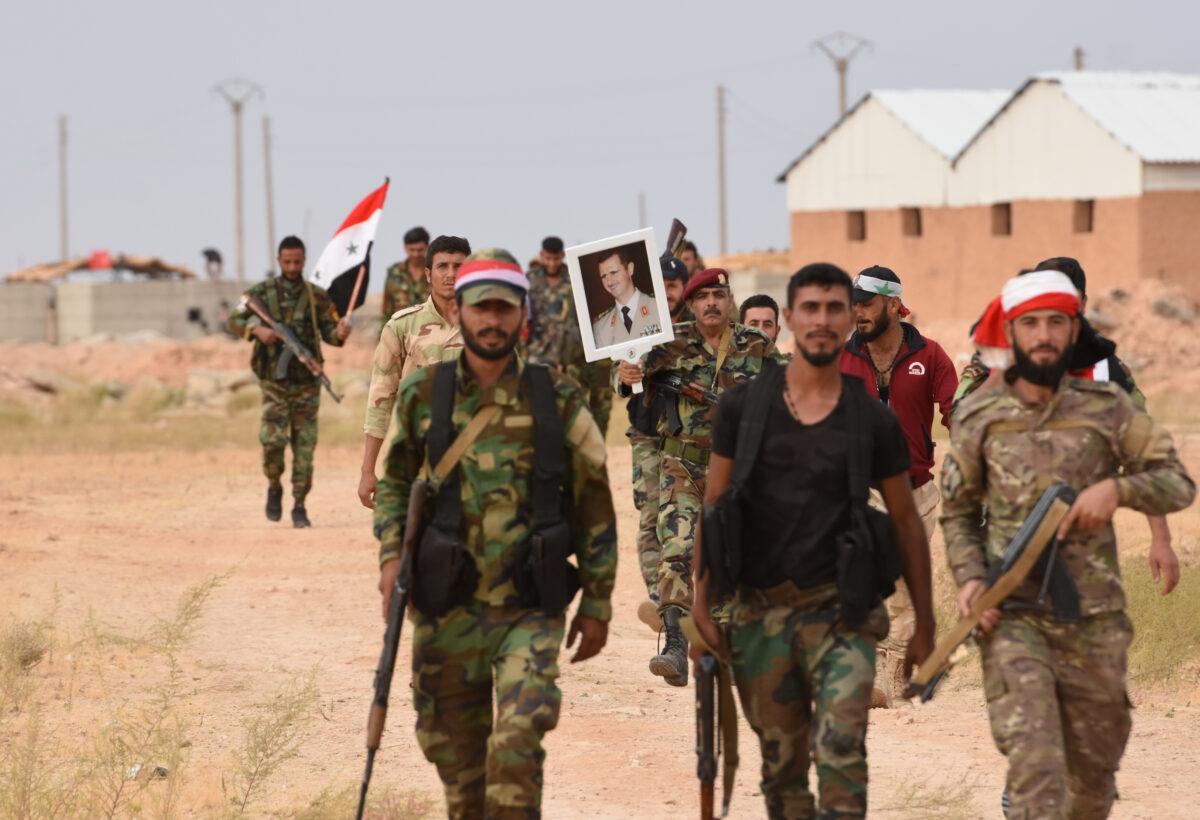 Syrian government forces raise a national flag and an image of President Bashar al-Assad at Tabqa air base in norther Syria's Raqa region on Oct.16, 2019. (AFP via Getty Images)