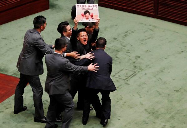 A pro-democracy lawmaker holding a placard is escorted by security from the Legislative Council, as Hong Kong's Chief Executive Carrie Lam takes questions from lawmakers regarding her policy address, in Hong Kong on Oct. 17, 2019. (Kim Kyung-Hoon/Reuters)