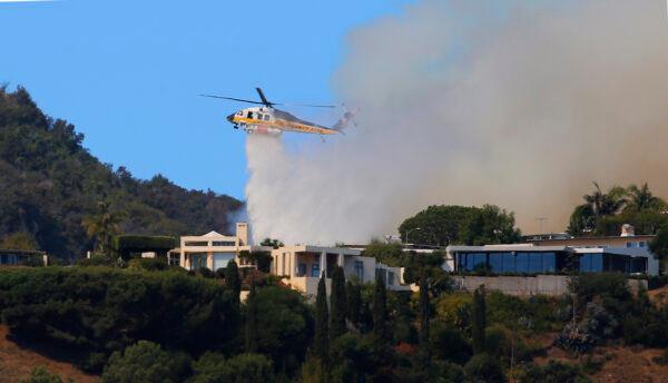 A helicopter makes a water drop as flames threaten homes on a ridgeline as a wildfire threatens homes in the Pacific Palisades area of Los Angeles on Oct. 21, 2019. (Reed Saxon/AP Photo)