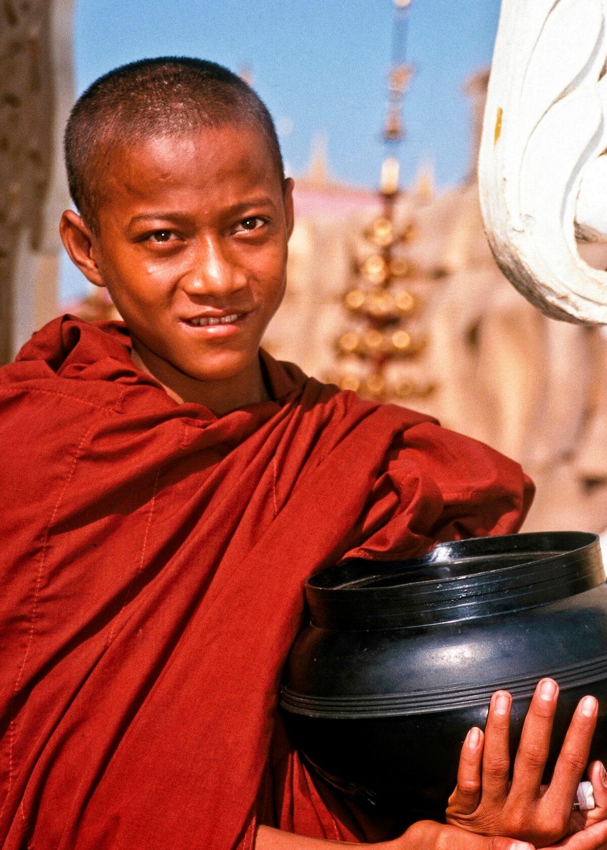 A young Buddhist monk, begging bowl in hand, standing near a pagoda in Yangon. (Fred J. Eckert)