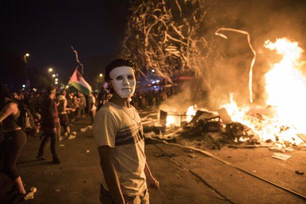 A masked anti-government protester stands by a burning barricade in Santiago, Chile, on Oct. 28, 2019. (Rodrigo Abd/AP Photo)
