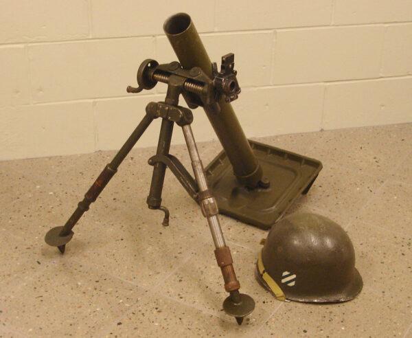 A WWII-era 60mm M2 mortar used by the United States infantry sits next to a helmet. (Curiosandrelics)