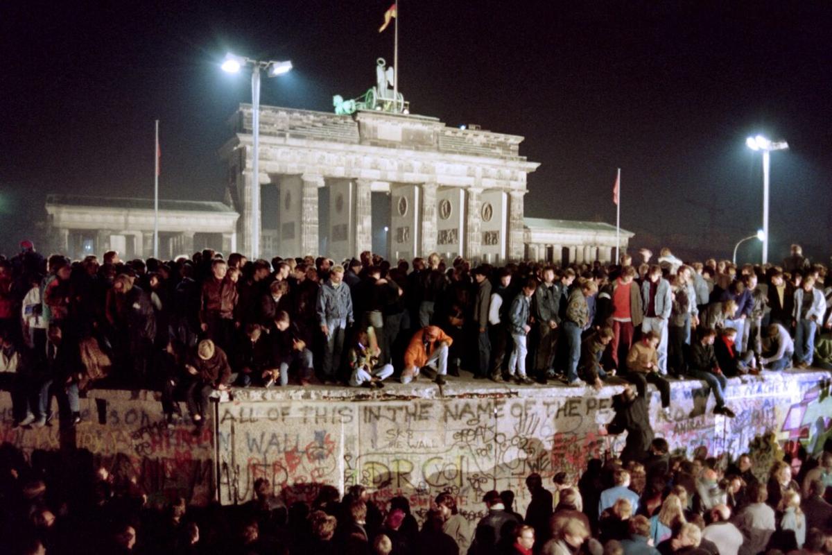 Thousands of young East Berliners crowd atop the Berlin Wall, near the Brandenburg Gate (background) on November 11, 1989. AFP PHOTO GERARD MALIE (Photo credit should read GERARD MALIE/AFP via Getty Images)
