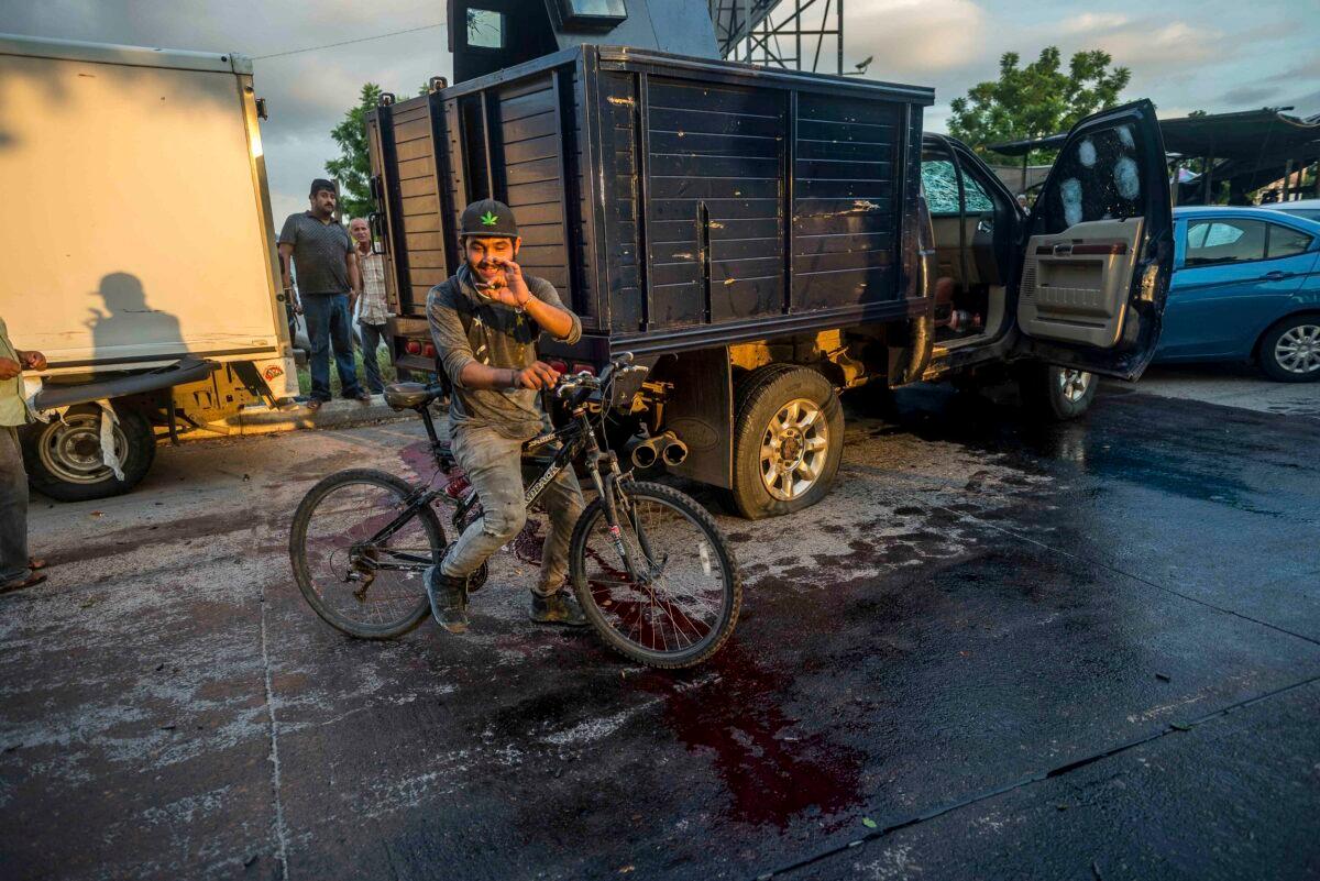 A man handles a bullet cartridge in a street by a truck with a flat tire and covered with bullets and blood after a gunfight in Culiacan, Mexico on Oct. 17, 2019. (Augusto Zurita/AP Photo)
