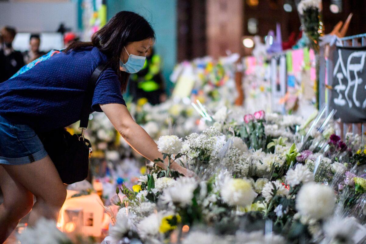 Mourners pay their respects next to flowers and a banner that reads “From all of us - God bless Chow Tsz-Lok” at the site where student Alex Chow, 22, fell during a recent protest in Kowloon, Hong Kong, on Nov. 8, 2019. (Anthony Wallace/AFP via Getty Images)