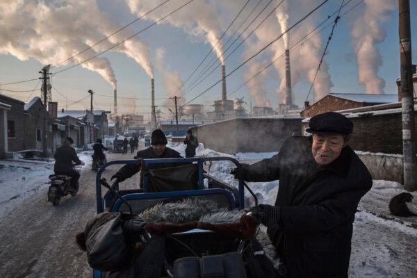 Smoke billows from stacks as Chinese men pull a tricycle in a neighbourhood next to a coal-fired power plant in Shanxi, China, on Nov. 26, 2015. (Kevin Frayer/Getty Images)