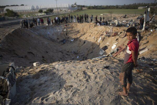 A barefoot Palestinian boy and others look into a crater made in overnight Israeli missile strikes that destroyed a house and killed eight members of the Abu Malhous family, in Deir al-Balah, central Gaza Strip on Nov. 14, 2019. (Khalil Hamra/AP Photo)