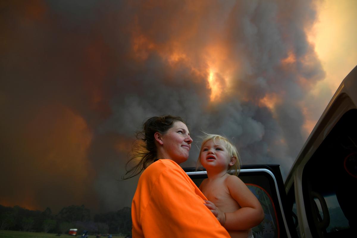 Sharnie Moren and her 18-month-old daughter Charlotte look on as thick smoke rises from bushfires near Nana Glen, near Coffs Harbour, Australia, on Nov. 12, 2019. (AAP Image/Dan Peled/via Reuters)