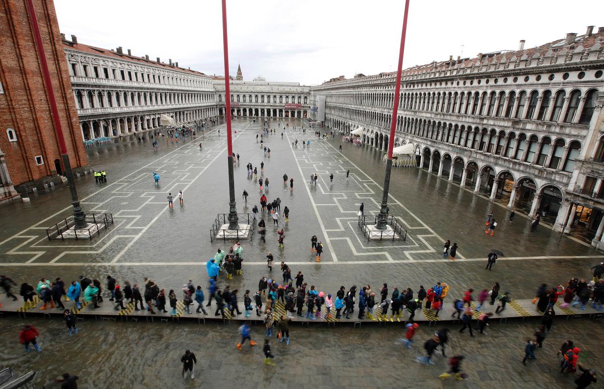 People walk in a flooded St. Mark's Square in Venice, Italy, on Nov. 12, 2019. (AP Photo/Luca Bruno)