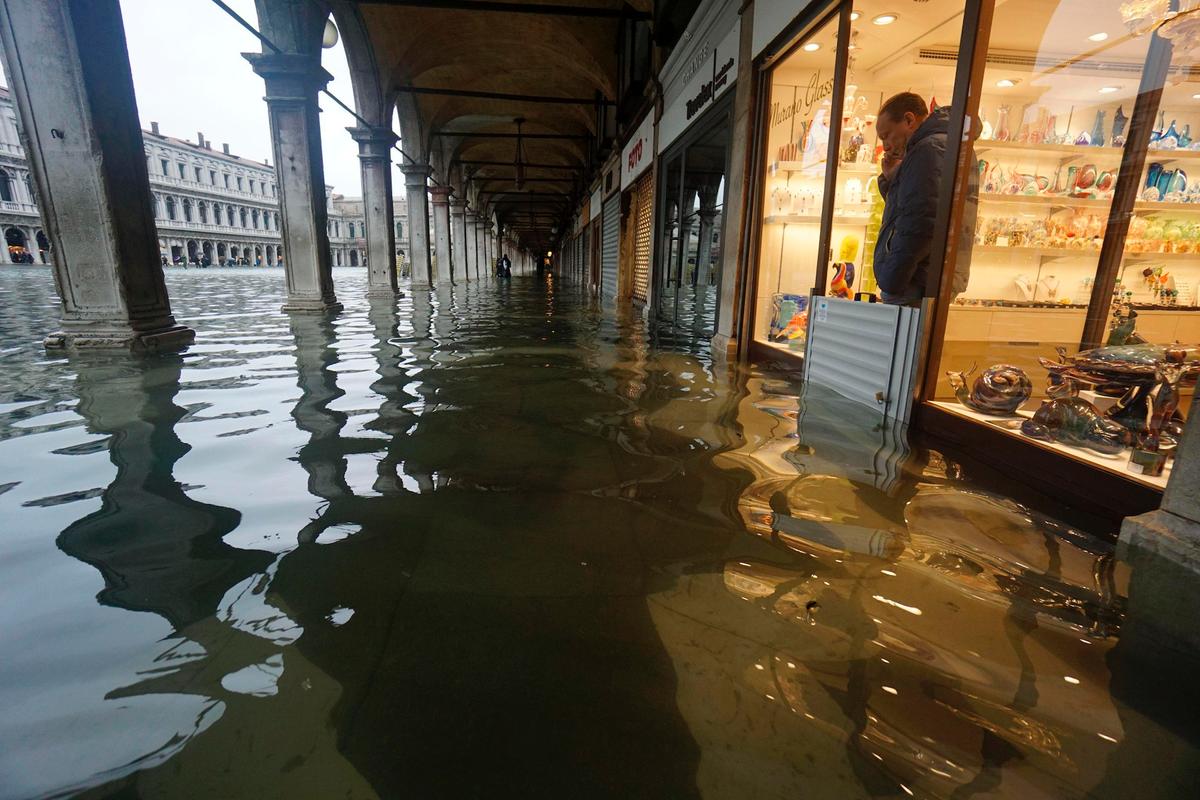 A shopkeeper looks out of his shop at a flooded St. Mark's Square on the occasion of a high tide, in Venice, Italy, on Nov. 12, 2019. (Andrea Merola/ANSA via AP)