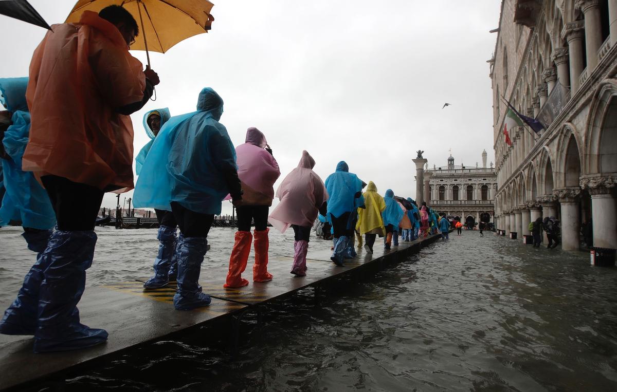 People walk on catwalk set up on the occasion of a high tide, in a flooded Venice, Italy, on Nov. 12, 2019. (AP Photo/Luca Bruno)